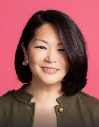 An asian woman smiling in front of a pink background.